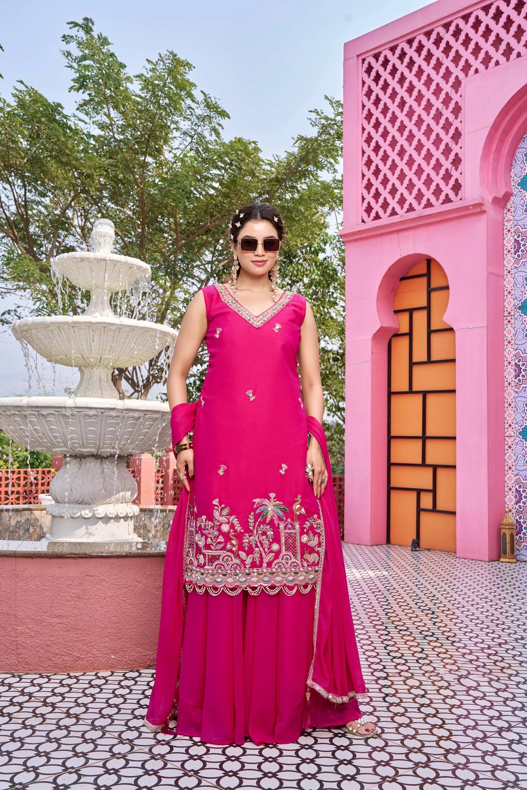 Woman in a pink traditional outfit standing in front of a pink architectural structure and fountain.